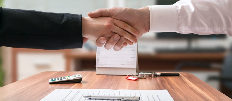 Shakehand of lawyer and business woman sitting behind desk with agreement.